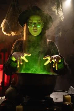 A realistic witch brewing a potion in a cauldron. She holds her hands over .. Stock Photos