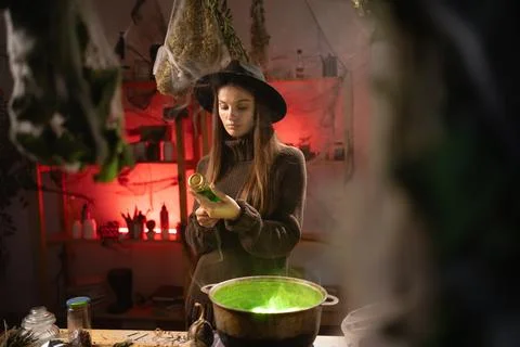 A realistic witch brewing a potion in a cauldron. holding jar of ingredient a Stock Photos