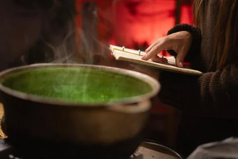 A realistic witch brewing a potion in a cauldron. A close-up shows her hands  Foto stock