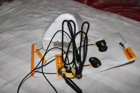 Realme wireless earbuds with charging cable and packaging on a bed Fotos Stock