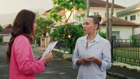 A realtor and her client are conversing in front of houses in an affluent Stock Footage 245642368