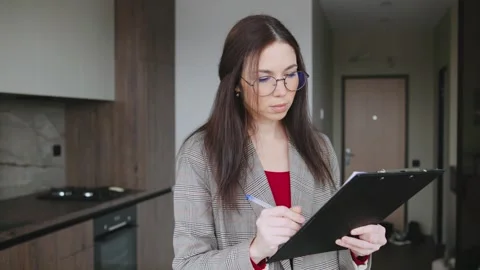 Realtor writes on a clipboard in a modern kitchen area with cardboard boxes Stock Footage 346224338