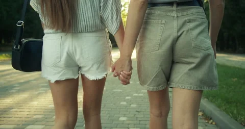 Rear close up view of two happy lesbian girls in shorts walking in the park and Stock Footage 283758010