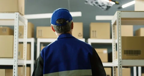Rear of gray-haired postman in blue uniform and cap walking in parcels passage 스톡 동영상 126601603