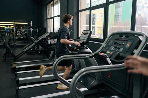 Rear remote view of athletic man jogging on gym machine, having cardio session Stock Photos