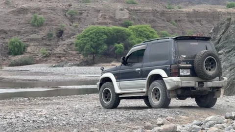 Rear shot of 4x4 SUV preparing to cross narrow stream of water in Balochistan Stock Footage 303472958