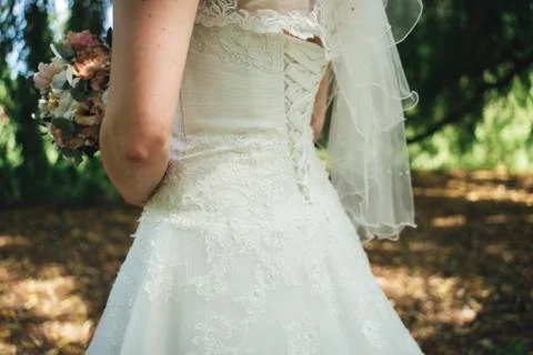 Rear side view on bride in white wedding dress holding wedding bouquet. Woman in Stock Photos