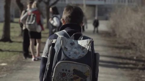 Rear side view of child carrying backpack going to or from school on outdoors Stock Footage 84909764