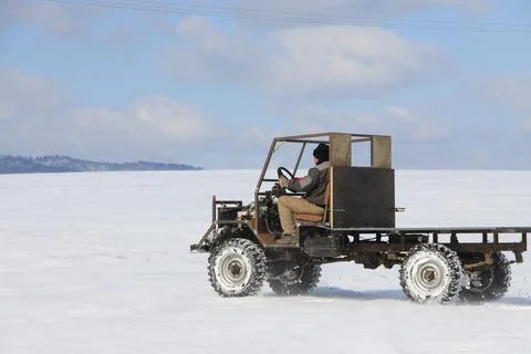 Rear side view of a man driving a homemade utility vehicle across a frozen, snow Stock Photos