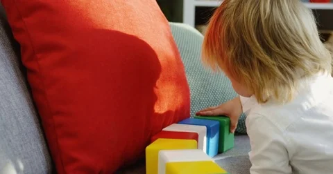 Rear of the small blonde boy playing with colourful kid's cubes on the couch in Stock Footage 82916661