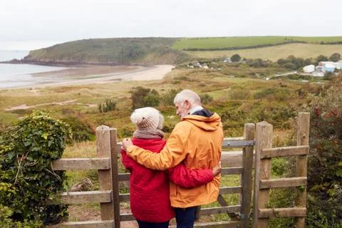 Rear View Of Active Senior Couple Looking Out Over Gate As They Walk Along Fotos Stock
