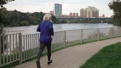 Rear view to active senior man in sport wear running near water canal Vídeos de archivo 116328015