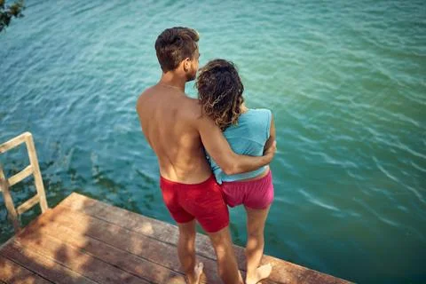 Rear view and high angle shot of couple in hug looking at beautiful blue wa.. Stock Photos