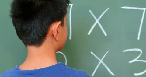 Rear view of Asian schoolboy solving math problem on chalkboard in classroom at Stock Footage 106930651