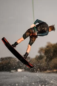 Rear view of athletic guy actively jumps on wakeboard holding rope in his hand. Foto stock