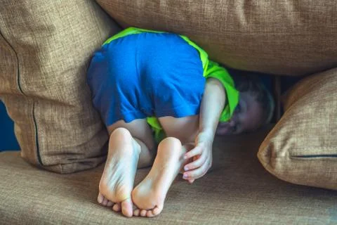 Rear view, back butt legs feet of a child hiding under a pillow, offended boy in Stock Photos