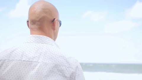 Rear view of bald man standing on the beach. He is looking at sea. Close up shot Stock Footage 113274445