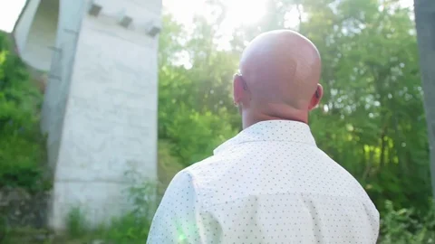 Rear view of a bald man standing under an abandoned bridge by the river. Medium Stock Footage 115025576