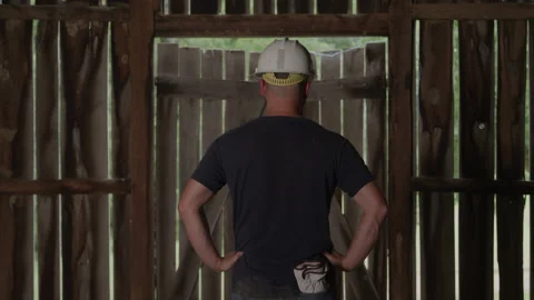 Rear view of Blue Collar Man in Hard Hat with Hands on Hips in Empty Barn Video stock 219580615