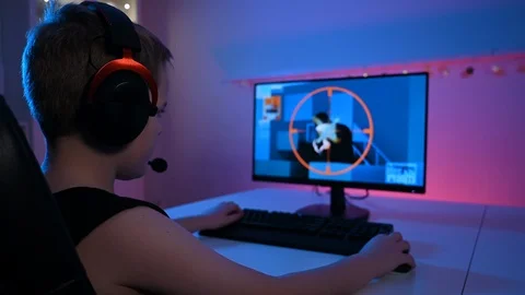 Rear view of boy with headset plays first person shooter video game on pc Stock Footage 100725167
