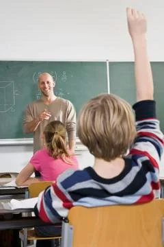 Rear view of a boy raising his hand in a classroom Stock Photos