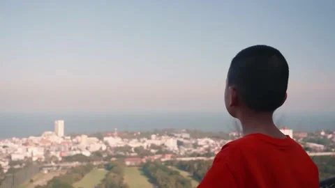 A rear view of a boy is standing at the viewpoint and looking at the cityscape. Stock Footage 145125607