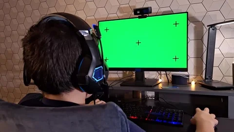 Rear view of boy uses a computer, sits with headphones in front of a green 스톡 동영상 273742695