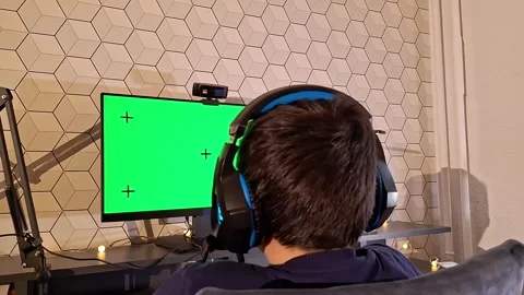 Rear view of boy uses a computer, sits with headphones in front of a green 스톡 동영상 277423569