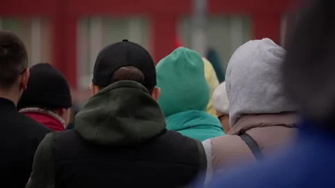 Rear view of a bundled crowd standing outdoors in an urban setting, wearing Stock Footage 317560628