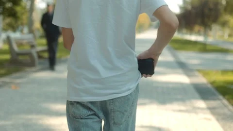 Rear view of a Casually Dressed adolescent Pulling Out Phone While Strolling Видео 331250922