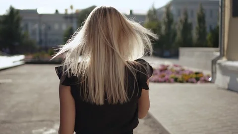 Rear view of charming long-haired blonde walking in city street turning around, Stock Footage 115103567