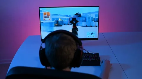 Rear view of child with headset plays first person shooter video game on pc Stock Footage 100725090