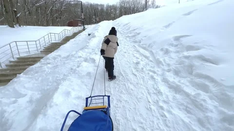 Rear view of a child in snowsuit pulling wooden sleds uphill on a winter day. Stock Footage 232886882