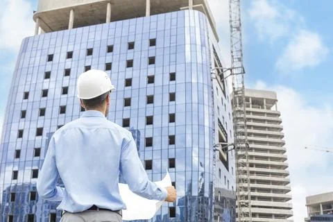 Rear view of construction engineer in helmet looking at plan of building to.. Stock Photos