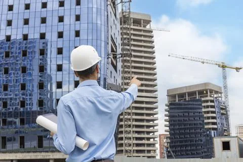 Rear view of construction engineer in helmet looking at plan of building to.. Stock Photos