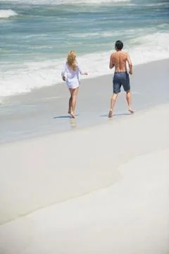 Rear view of a couple running on the beach Stock Photos