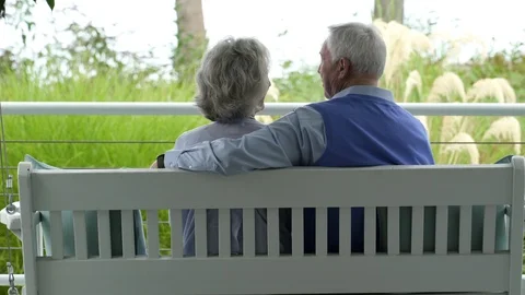 Rear view of couple sitting on bench on porch together chatting. 動画素材 88019585