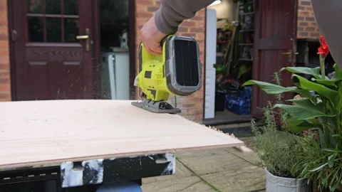 Rear view of a craftsman using a battery powered Jigsaw cutting a board on .. Stock Footage 321001282