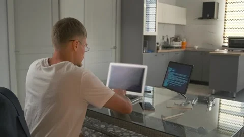 Rear view. Developer edits code on a laptop while checking specs on a tablet. Stock Footage 296220904