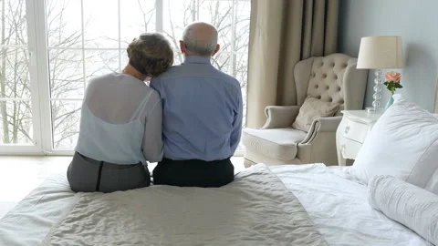 Rear view elderly couple sitting in bedroom, embracing and looking the window Stock-Footage 99740306