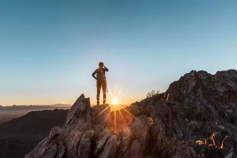 Rear view of female hiker standing on cliff against clear sky during sunrise Stock Photos