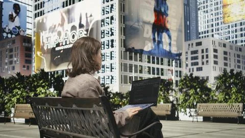 Rear view of female programmer on park bench writing code on laptop Stockfoto's