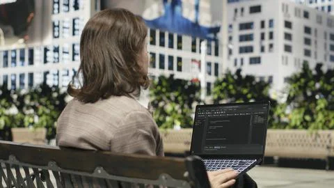 Rear view of female programmer on park bench writing code on laptop 库存照片