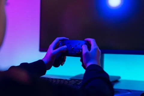 Rear view of gamer holding controller in dark room with blank monitor scree.. Stock Photos