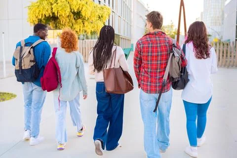Rear view group of students smiling and walking together outdoors with notebooks Stock Photos