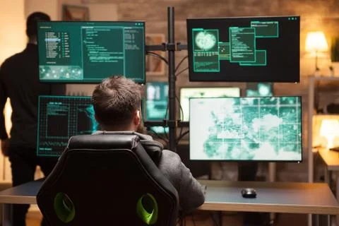 Rear view of hacker in front of computer with multiple screens Stock Photos