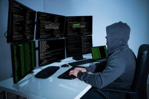 Rear view of hacker using computers to steal data in office Stock Photos