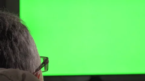 Rear view of the head of an older white man with glasses in front of a green TV Stock Footage 250019097