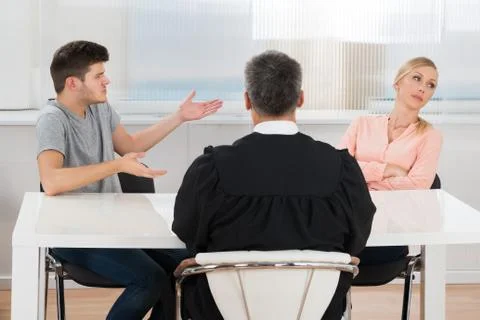 Rear View Of Judge Sitting In Front Of A Young Couple Having Conflict In Cour Stock Photos