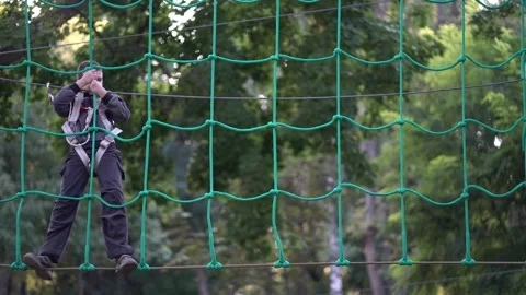 Rear view of a kid climbing a green rope structure and chain walkway in a wooded Stock Footage 345285652